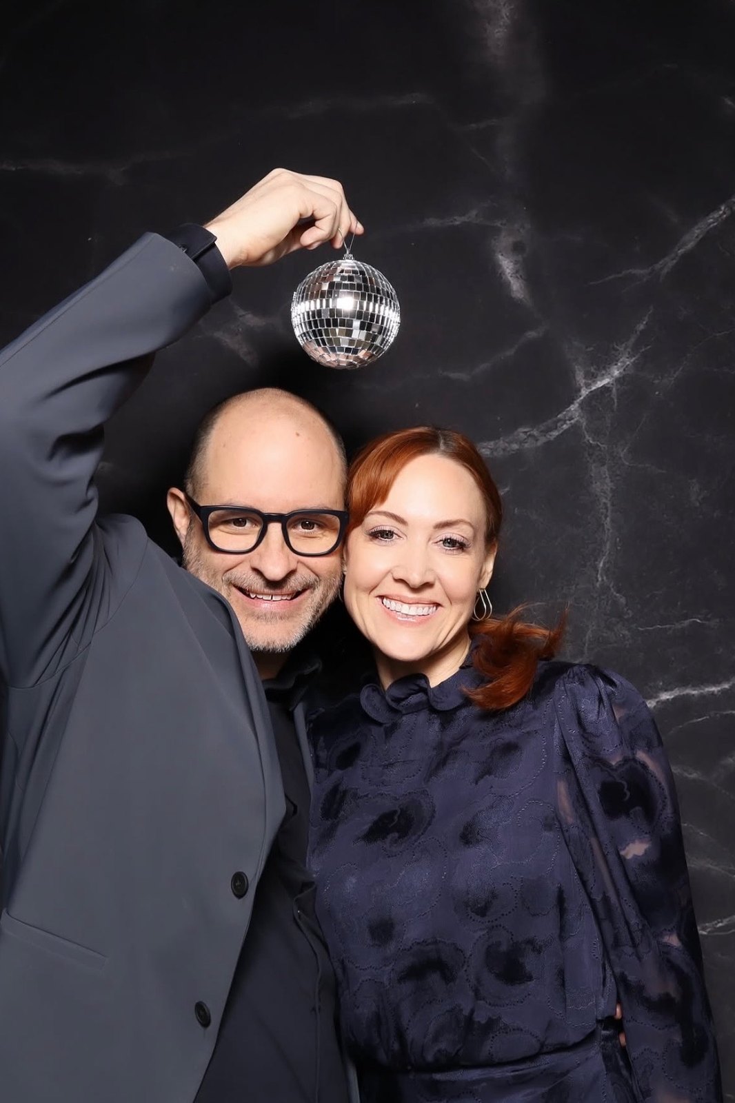 Two guests posing with a disco ball in front of a black marble backdrop.