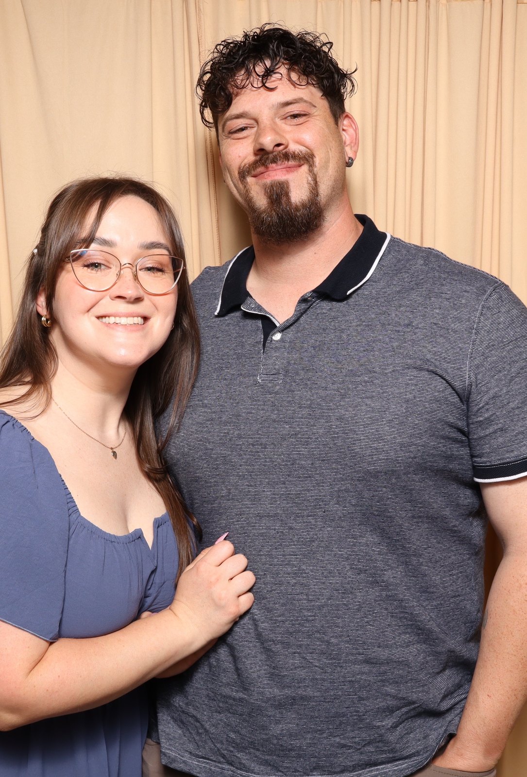 A couple posing together in front of a champagne coloured backdrop.