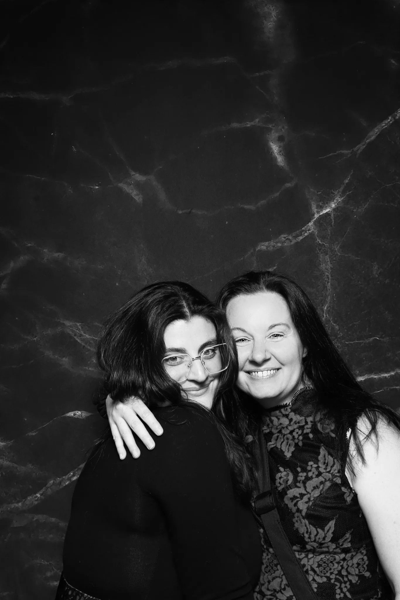 A black and white portrait of two guests against a marble backdrop.