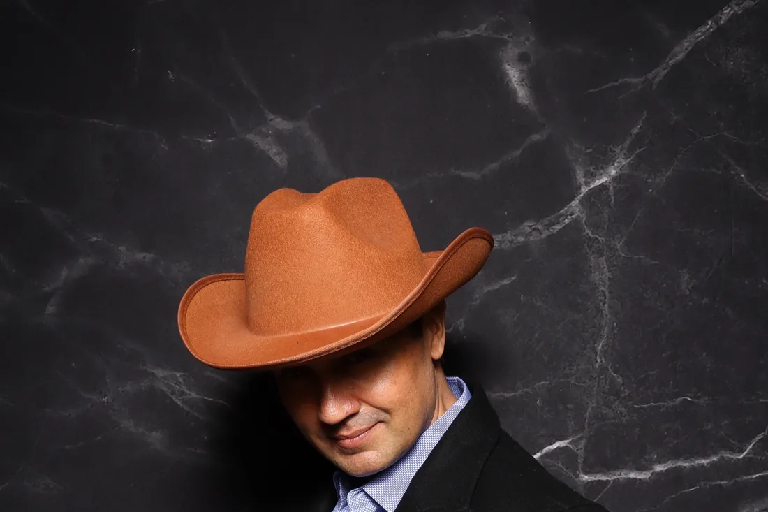 A guest in a wide brim hat photographed against a black marble backdrop.